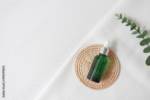 Dropper bottle serum on wood plate. Natural facial essential oil or serum packaging on white fabric background. Beauty product branding mock-up.  Cosmetic skincare concept. top view
