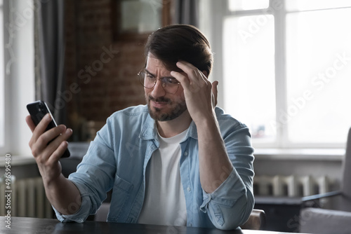 Bilde på lerret Concerned annoyed smartphone user man staring at cellphone screen with upset fac