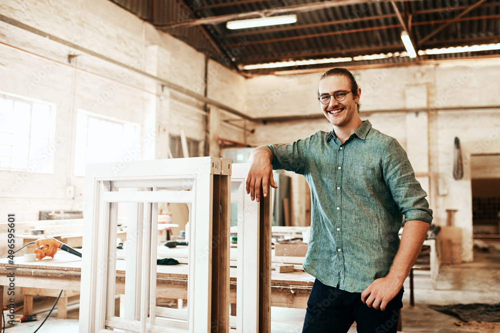 I just love creating pieces of art from wood. Portrait of a happy young carpenter posing inside a workshop.