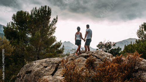 Junges verliebtes paar Hand in Hand auf Felsen mit Blick in die Berglandschaft und dramatischen Wolken auf mallorca