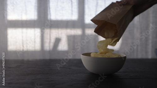 Fototapeta Naklejka Na Ścianę i Meble -  pour potato chips from paper bag into white bowl on oak table