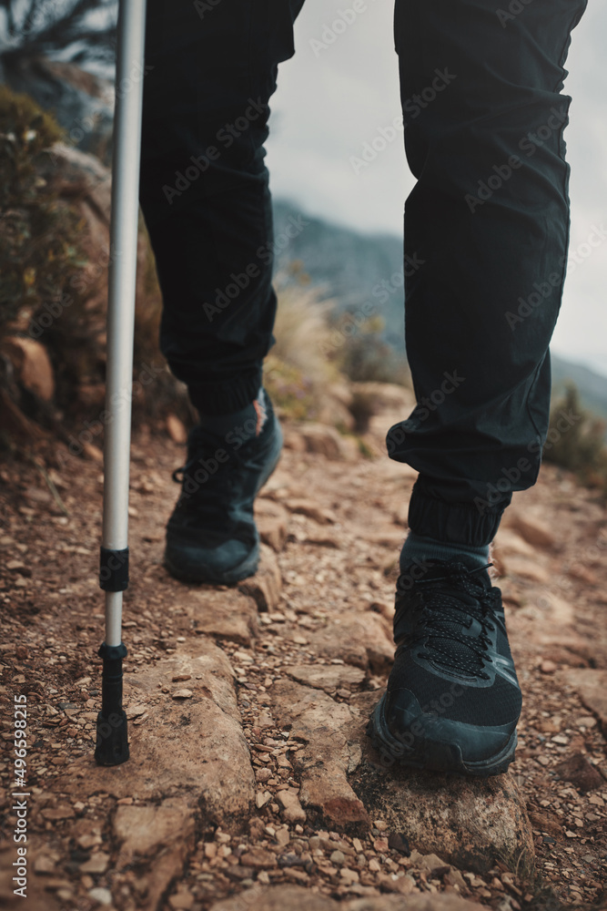 Fresh air and muddy boots make everything better. Closeup shot of an unrecognisable man using a walking pole while hiking through the mountains.