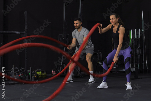Athletic young couple with battle rope doing exercise in functional training fitness gym. © ty