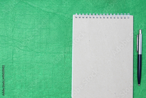 White and gray notepad sheet with spiral with pen against the background of green fabric. Concept of analysis, study, attentive work. Stock photo with empty place for your text and design.