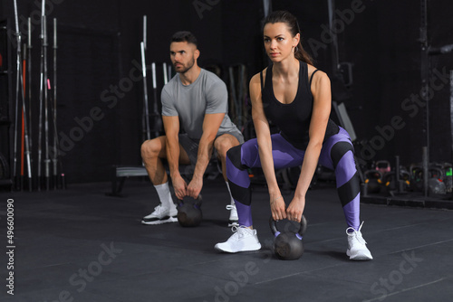 Fit and muscular couple focused on lifting a dumbbell during an exercise class in a gym.