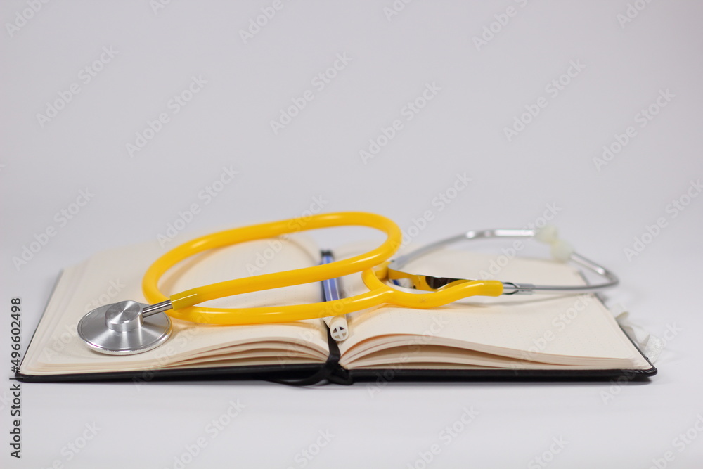 A medical stethoscope with a yellow heart on an open notebook with a blue pen for medical concept A medical stethoscope with a yellow heart on an open notebook with a blue pen for medical concept