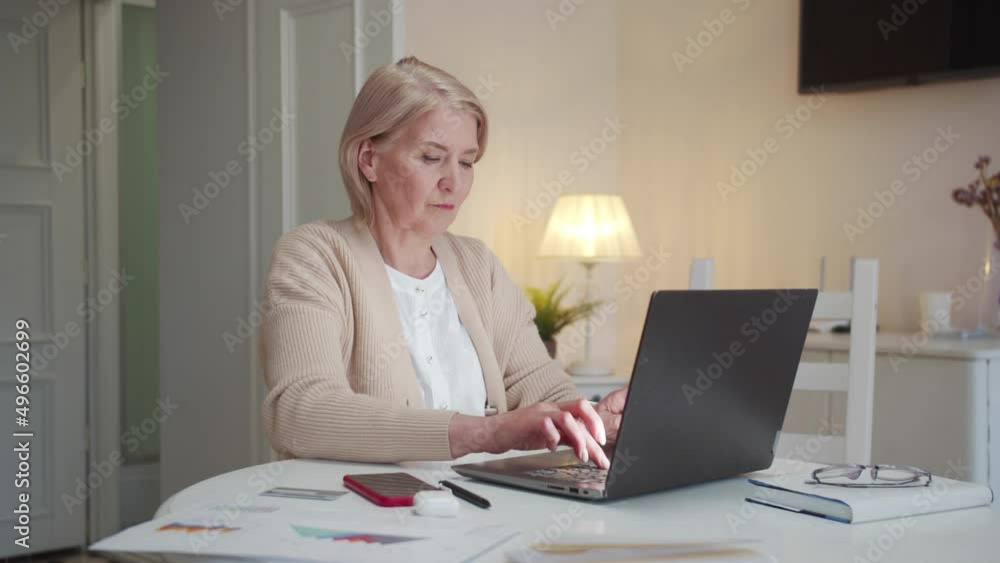 An old woman works at a computer. She is sitting at the table and typing slowly An old woman works at a computer. She is sitting at the table and typing slowly