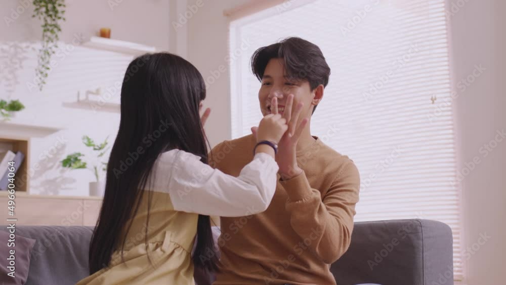 Asian father teaches daughter to play games and do activities on the sofa on vacation.