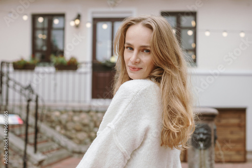 Portrait of young beautiful blue-eyed woman with long hair looking at camera feeling happy. Outdoors, old town.