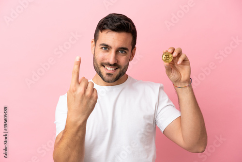 Young man holding a Bitcoin isolated on pink background doing coming gesture © luismolinero