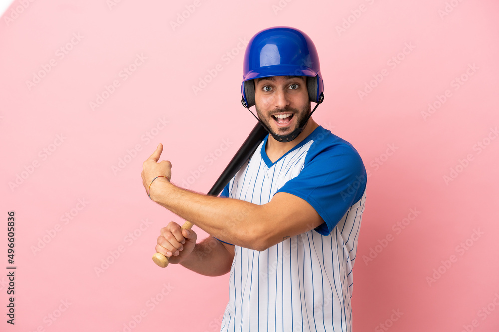 Baseball player with helmet and bat isolated on pink background pointing back Baseball player with helmet and bat isolated on pink background pointing back
