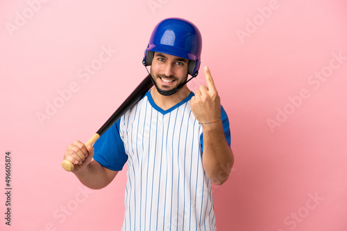Baseball player with helmet and bat isolated on pink background doing coming gesture