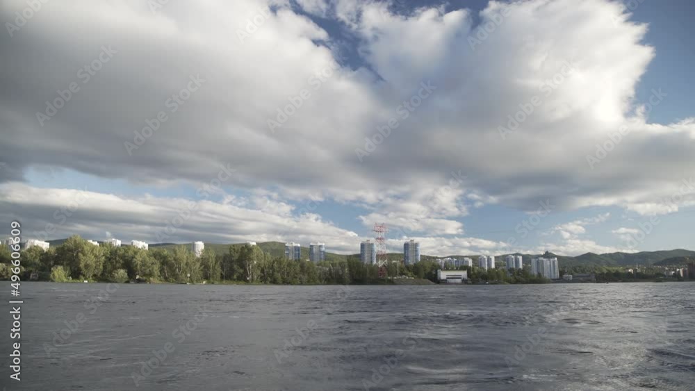 Driving motorboat on blue river near coastline of city with tall houses. Speedboat riding fast creating waves and trail. Point of view speedboat floating on river on background of blue sky with clouds Driving motorboat on blue river near coastline of city with tall houses. Speedboat riding fast creating waves and trail. Point of view speedboat floating on river on background of blue sky with clouds