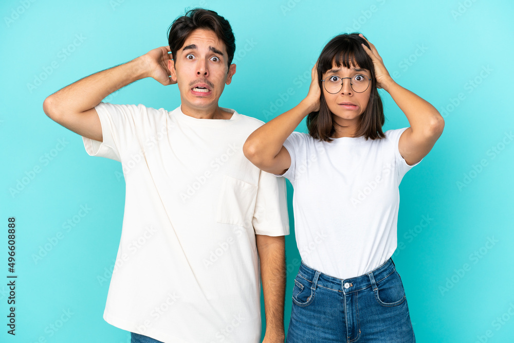 Young mixed race couple isolated on blue background takes hands on head because has migraine Young mixed race couple isolated on blue background takes hands on head because has migraine