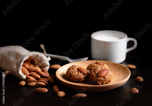 Almond cookies in wooden bowl and healthy milk on old black wooden floor Almonds and seeds in freely arranged sacks Delicious organic pastries photo