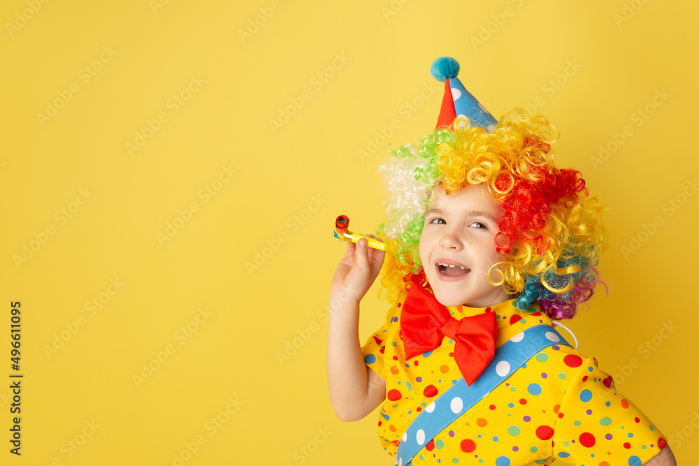 Funny kid clown against yellow background. Happy child playing with festive decor. Birthday and 1 April Fool's day concept Funny kid clown against yellow background. Happy child playing with festive decor. Birthday and 1 April Fool's day concept