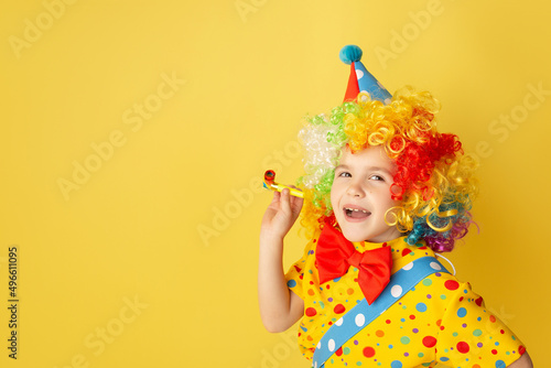 Funny kid clown against yellow background. Happy child playing with festive decor. Birthday and 1 April Fool s day concept