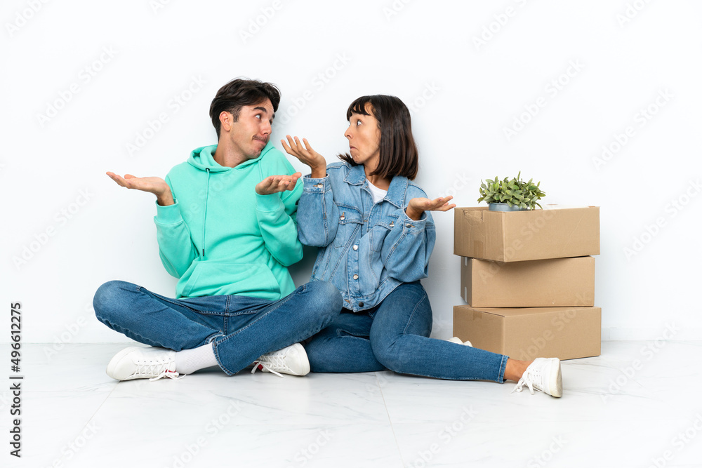 Young couple making a move while picking up a box full of things sitting on the floor isolated on white background making unimportant gesture while lifting the shoulders Young couple making a move while picking up a box full of things sitting on the floor isolated on white background making unimportant gesture while lifting the shoulders