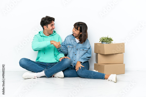 Young couple making a move while picking up a box full of things sitting on the floor isolated on white background handshaking after good deal