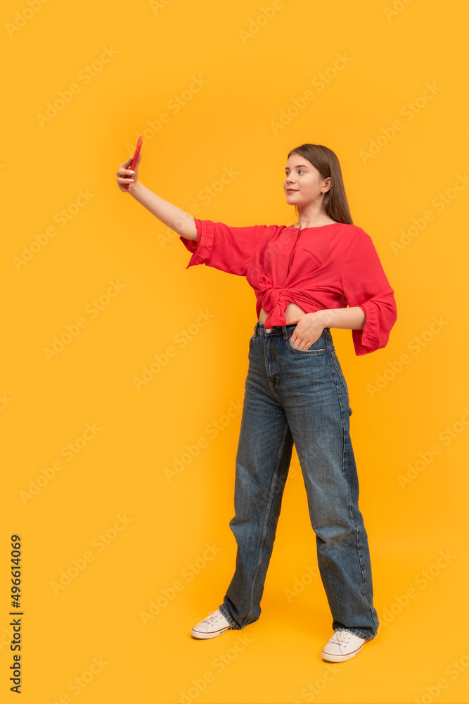 Full-leigh portrait of teenager with phone on bright yellow background. Young girl takes selfie of herself. Schoolgirl blogger. Full-leigh portrait of teenager with phone on bright yellow background. Young girl takes selfie of herself. Schoolgirl blogger.