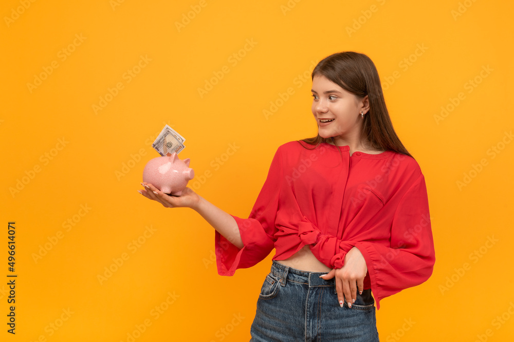 Young woman or girl holds piggy bank with money in hands and looks at it in surprise. Financial literacy concept. Young woman or girl holds piggy bank with money in hands and looks at it in surprise. Financial literacy concept.