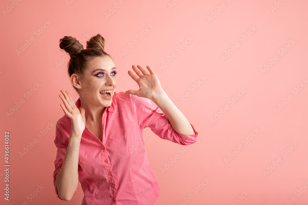 Cheerful surprised young woman with two bun hairstyles looks to the side on a pink background. Adults are like children. Pink mood. Cheerful surprised young woman with two bun hairstyles looks to the side on a pink background. Adults are like children. Pink mood.