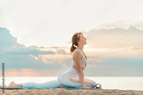 Attractive woman practicing yoga outdoors by the sea. Young beautiful girl doing sports and yoga on the beach.