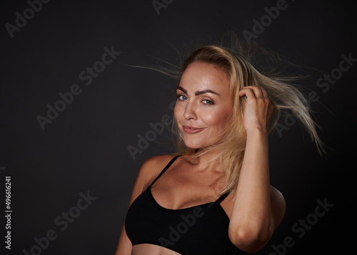 Confident smiling beautiful fitness young Caucasian woman with a healthy toned body, clean glowing tanned skin posing in a black bra against colored background with copy ad space