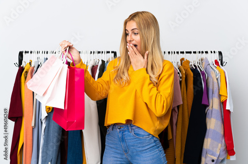 Young Uruguayan blonde woman in a clothing store and holding shopping bags with surprise and shocked facial expression