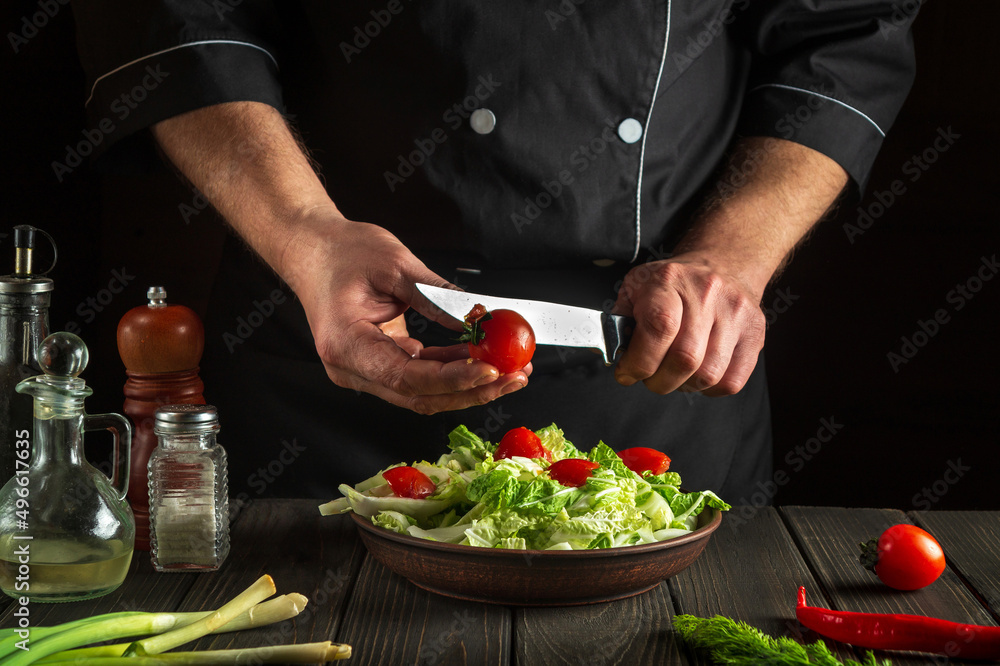 Professional chef prepares a vegetable salad in the kitchen. Cutting a fresh tomato for a vitamin salad with a knife. Vegetarian cuisine