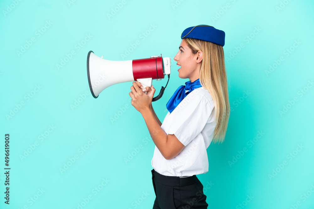 Airplane stewardess Uruguayan woman isolated on blue background shouting through a megaphone Airplane stewardess Uruguayan woman isolated on blue background shouting through a megaphone