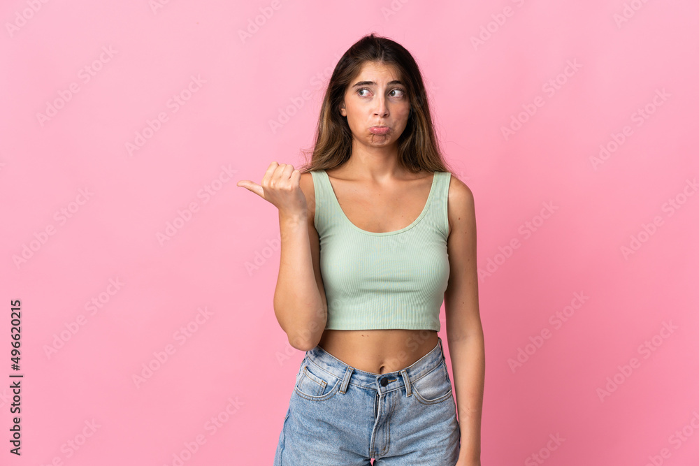 Young caucasian woman isolated on pink background unhappy and pointing to the side Young caucasian woman isolated on pink background unhappy and pointing to the side