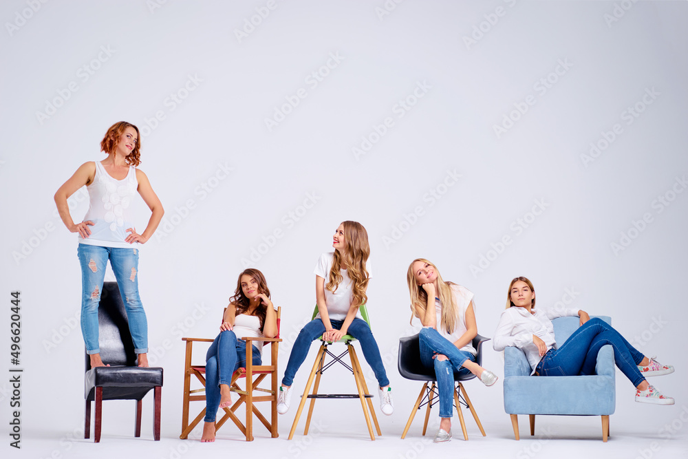 Naklejka premium Studio portrait of happy five pretty young women sitting on chairs. White background.