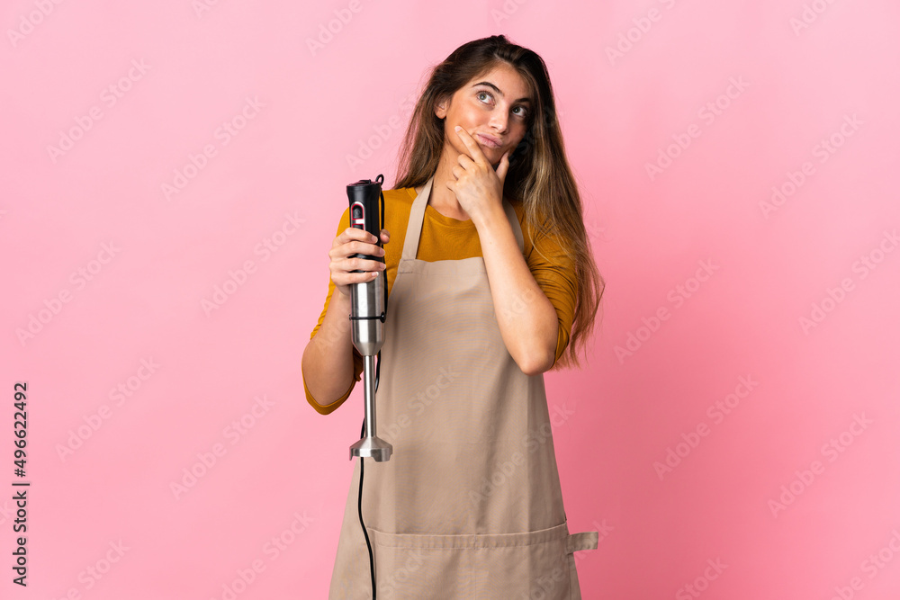 Young chef woman using hand blender isolated on pink background having doubts Young chef woman using hand blender isolated on pink background having doubts