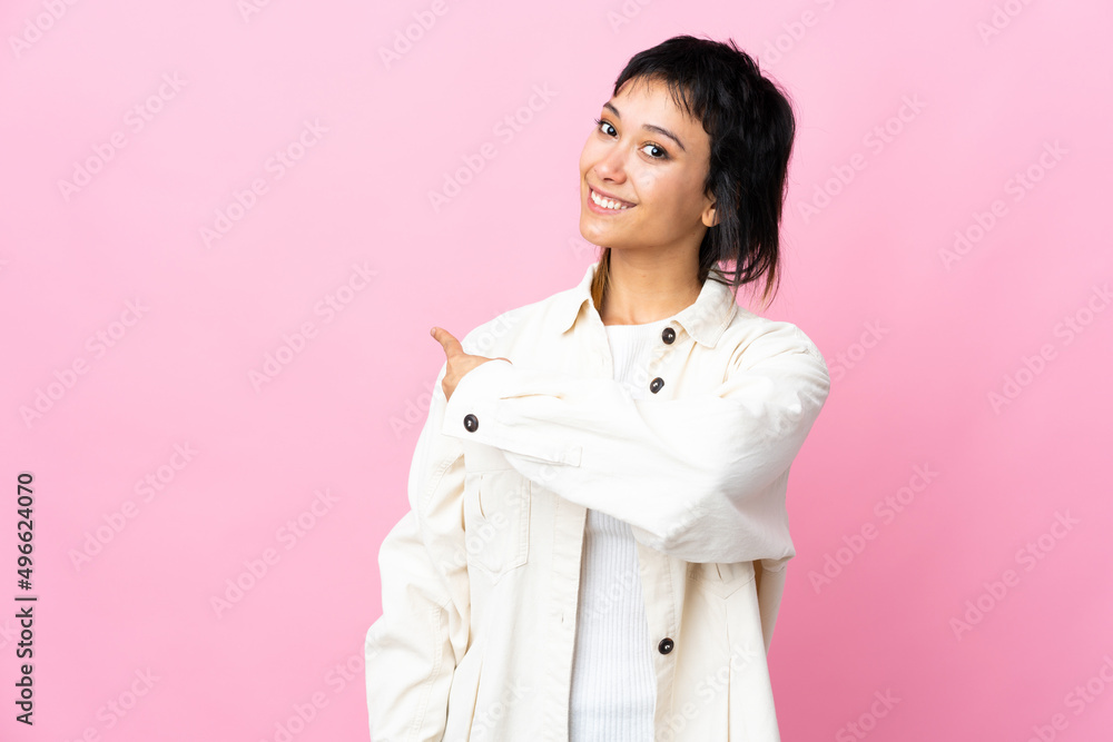 Young Uruguayan woman over isolated pink background pointing back Young Uruguayan woman over isolated pink background pointing back