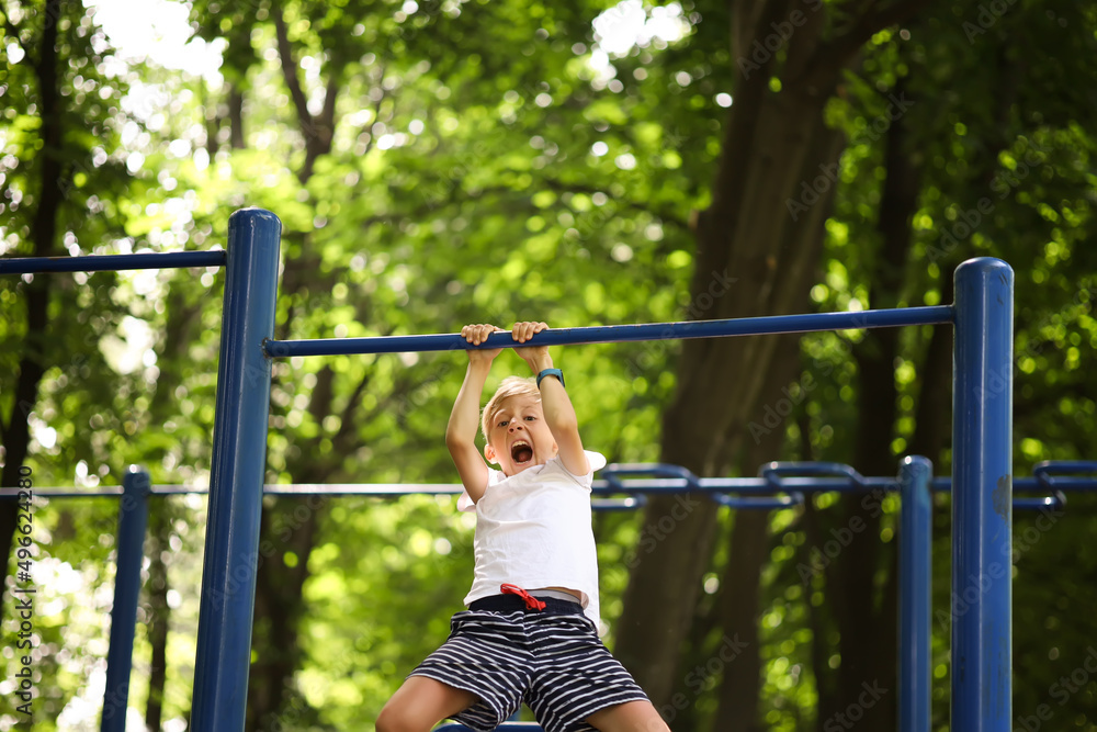 the boy goes in for sports in the park hangs on the horizontal bar pulls himself up and shouts loudly