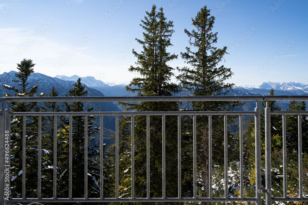 Iron railings on a viewing platform with a view of lightly snow covered fir trees and mountains on a sunny day in winter
