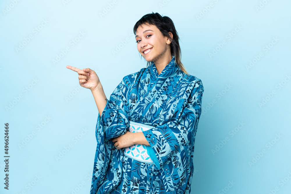 Young woman wearing kimono over isolated blue background pointing finger to the side Young woman wearing kimono over isolated blue background pointing finger to the side