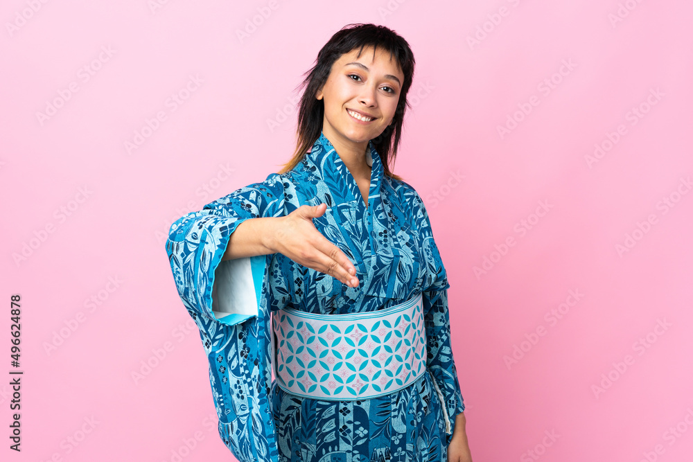 Young woman wearing kimono over isolated blue background shaking hands for closing a good deal Young woman wearing kimono over isolated blue background shaking hands for closing a good deal