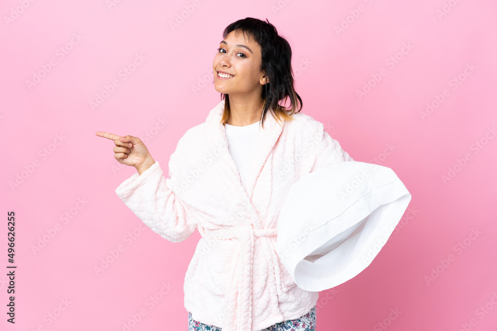 Young Uruguayan woman in pajamas over isolated pink background pointing finger to the side Young Uruguayan woman in pajamas over isolated pink background pointing finger to the side