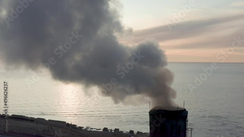 The coal processing factory pollutes the environment with the release of toxic gases. Evening sunset and blue sea Drone removes the chimney releases black smoke.