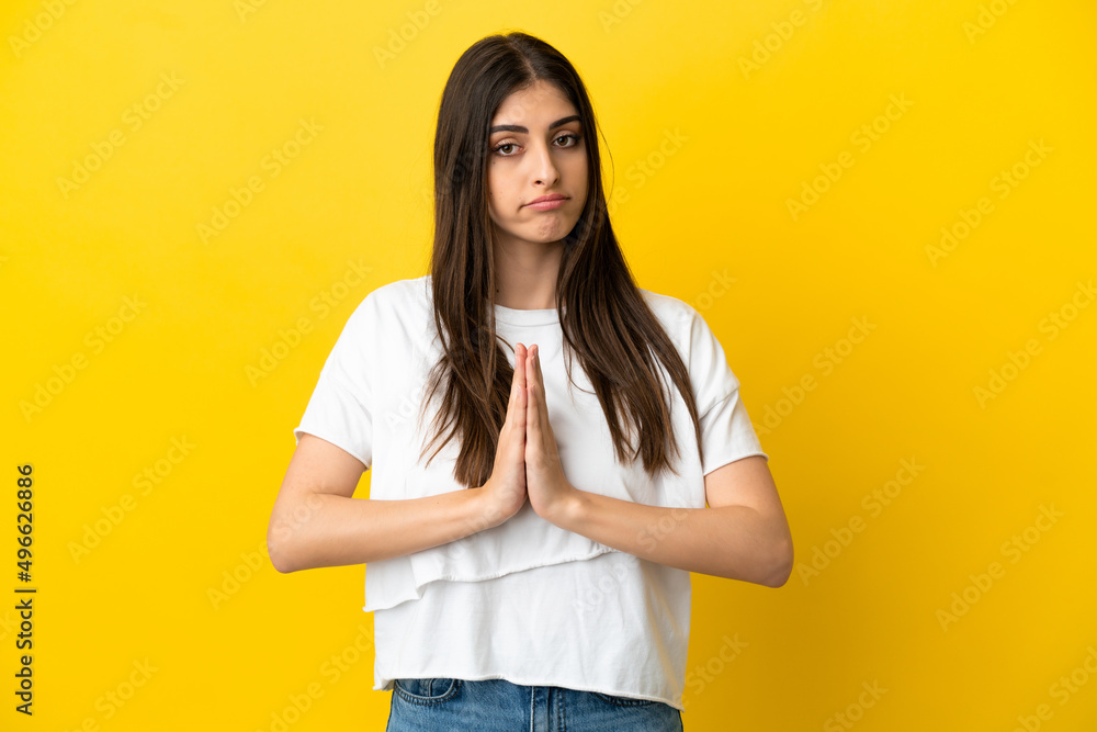 Young caucasian woman isolated on yellow background keeps palm together. Person asks for something Young caucasian woman isolated on yellow background keeps palm together. Person asks for something