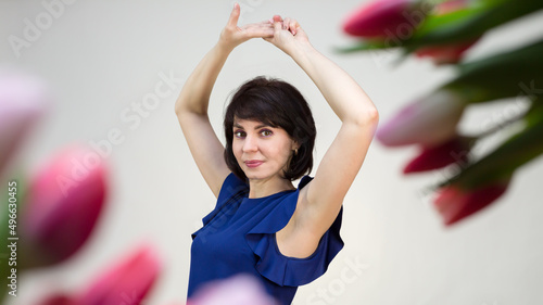 An adult brunette in a blue blouse on a white background with tulips beautifully raised her hands up.