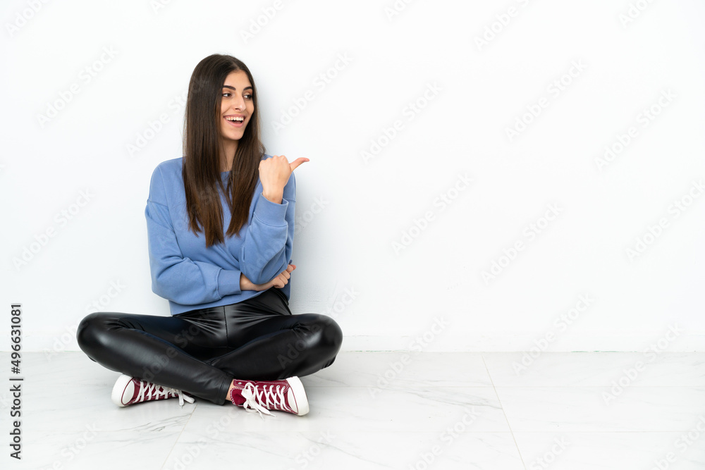 Young woman sitting on the floor isolated on white background pointing to the side to present a product Young woman sitting on the floor isolated on white background pointing to the side to present a product