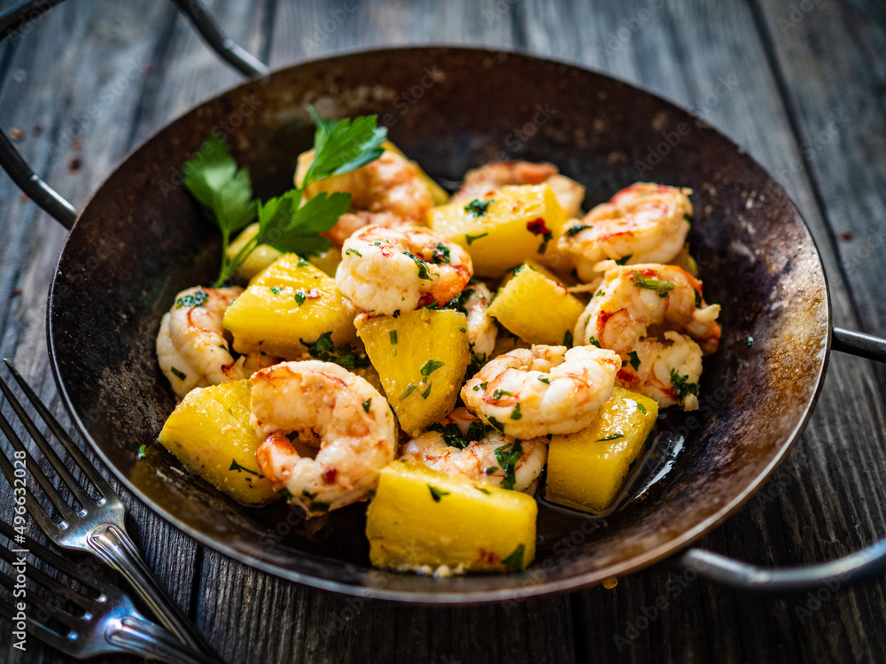 Fried prawns and pineapple in frying pan on wooden table
Fried prawns and pineapple in frying pan on wooden table