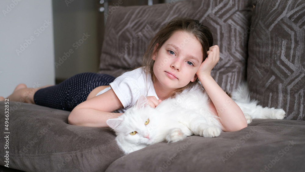 Little happy blonde girl lies on the bed and hugs a white sleeping kitten and smiles closing her eyes Little happy blonde girl lies on the bed and hugs a white sleeping kitten and smiles closing her eyes