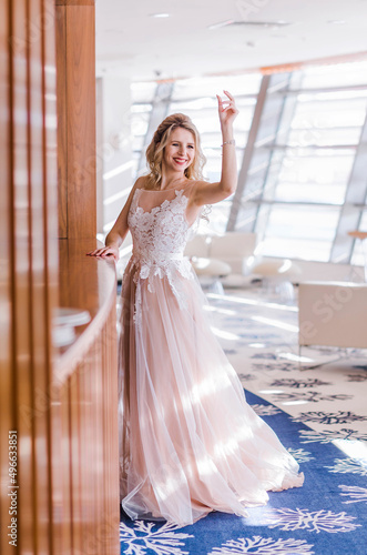 Bride in a long light pink wedding dress posing in a bright hotel lobby