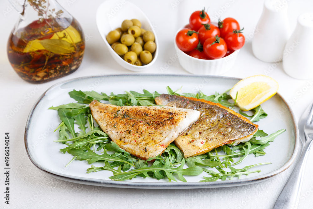 Fried dorado fillet with crispy skin. Arugula, cherry tomatoes, olives, lemon and olive oil. Traditional Mediterranean dish. White background. Selective focus, close-up. Fried dorado fillet with crispy skin. Arugula, cherry tomatoes, olives, lemon and olive oil. Traditional Mediterranean dish. White background. Selective focus, close-up.