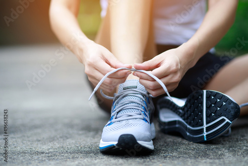 Fototapeta Naklejka Na Ścianę i Meble -  Running shoes. close up female athlete tying laces for jogging on road. Runner ties getting ready for training. Sport lifestyle. copy space banner.