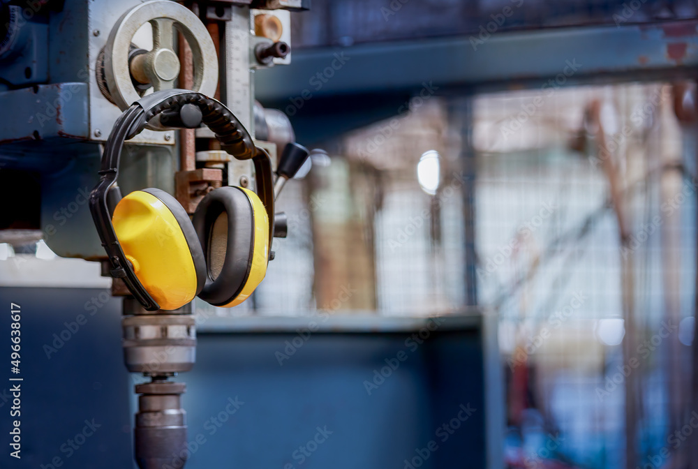 Yellow protective ear muffs hang on machines in heavy industrial plants. - obrazy, fototapety, plakaty 